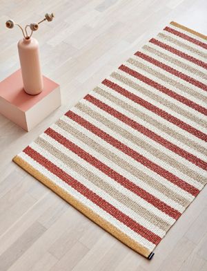 Der Teo Brick Teppich zeigt ein lebhaftes Streifenmuster, das in Ziegelrot, Beige und Vanille gewebt ist.