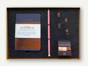 Geschenkbox mit Notebook, Papierklammern, Tapes und Bleistift